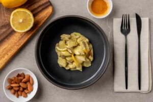 piatto con pollo allo zafferano, con spicchi di limone e scaglie di mandorle, circondato da prodotti freschi, mandorle sgusciate, polvere di zafferano e limone. il piatto è preparato da liffo in autonomia, personal chef con intelligenza artificiale, per un contorno pronto quando torni a casa dal lavoro