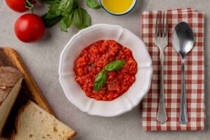 piatto di pappa al pomodoro circondato da ingredienti freschi, pomodoro cuore di bue, basilico, pane e olio